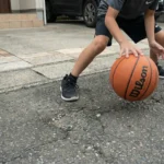 自宅の駐車場のアスファルトでバスケットボールをドリブルする子供の写真。